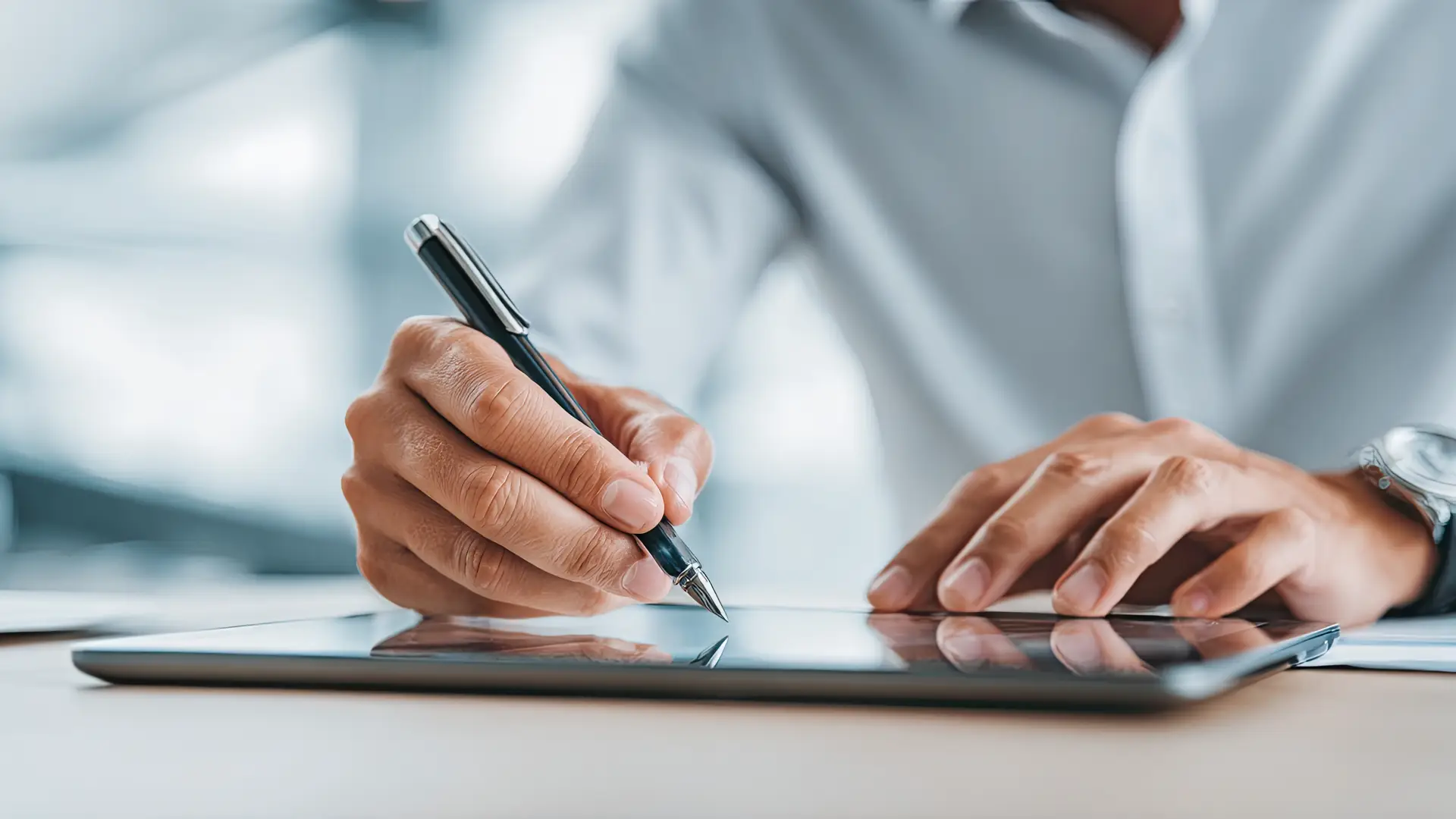 Homem escrevendo em um tablet com caneta em mesa de madeira