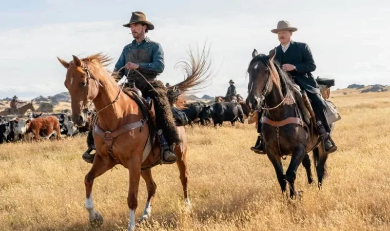Cena do filme Ataque dos Cães, com dois homens montados a cavalo em um campo aberto de pasto dourado sob luz do sol.