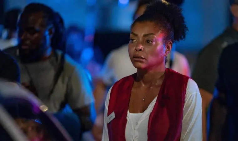 Cena do filme Até a Última Gota, mostrando uma mulher com expressão séria usando colete vermelho em um ambiente escuro e iluminado por luz azul. 