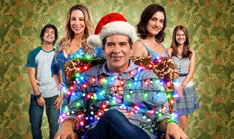 Cena do filme Tudo Bem no Natal que Vem, mostrando Leandro Hassum vestido de Papai Noel com luzes de Natal ao redor, cercado por sua família