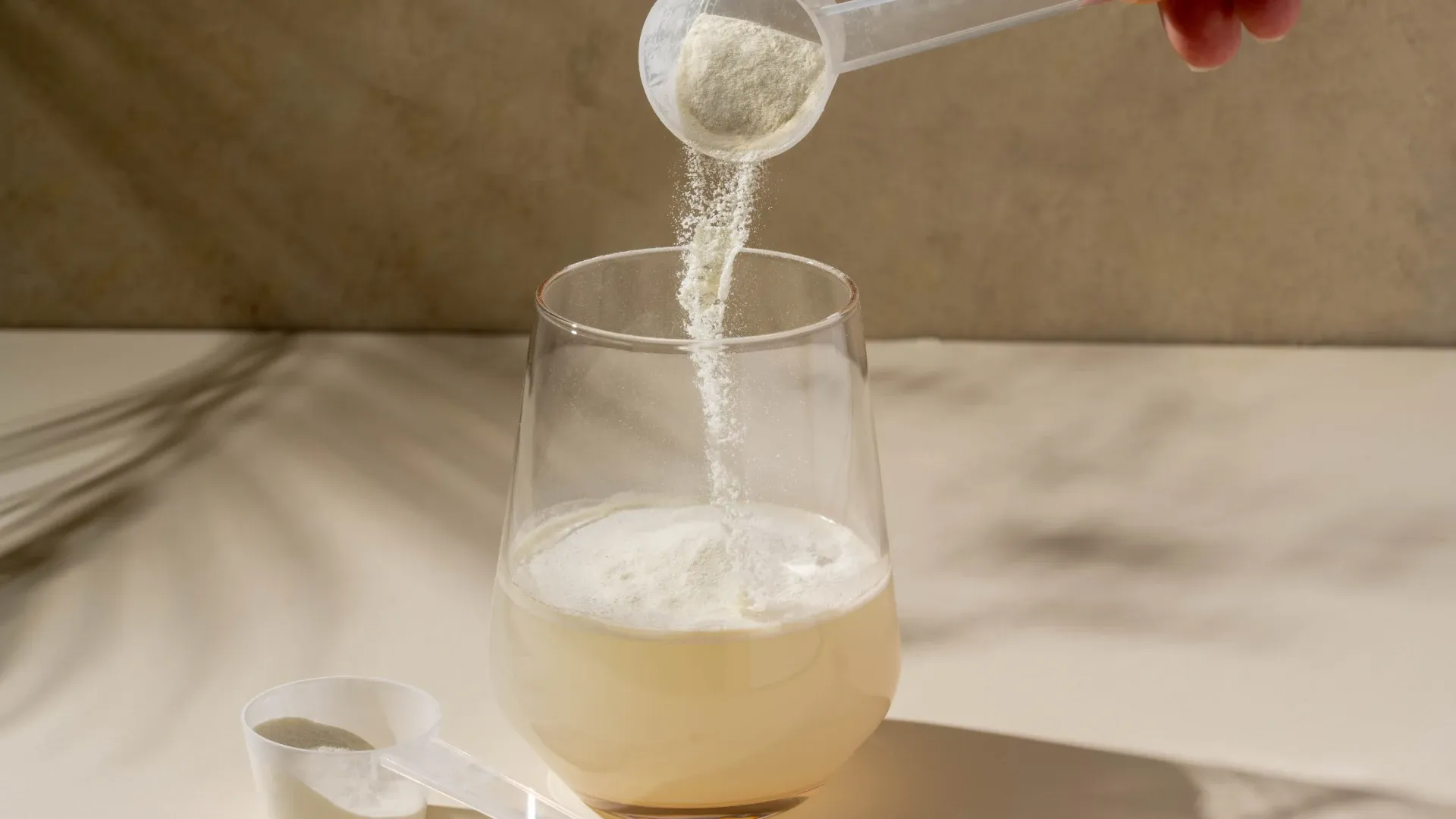 Dosador de creatina cheio e um copo d'água transparente com outro dosador do lado