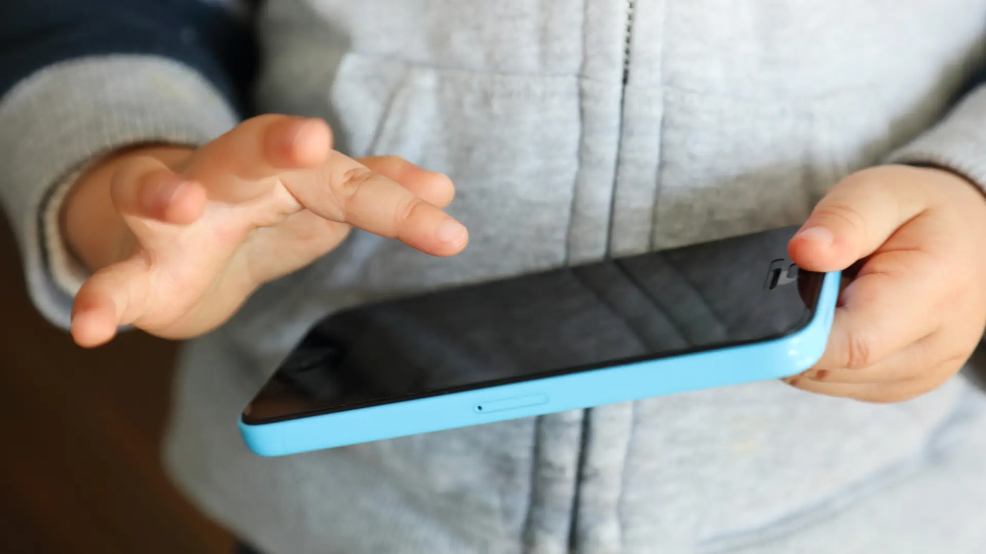 Imagem mostra uma criança segurando um iPhone com as duas mãos