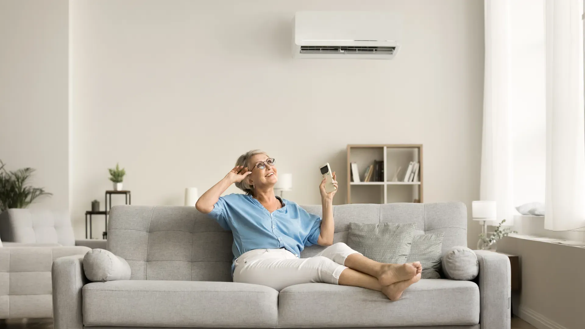 Senhora sentada no sofá sorrindo e com o controle remoto do ar-condicionado na mão