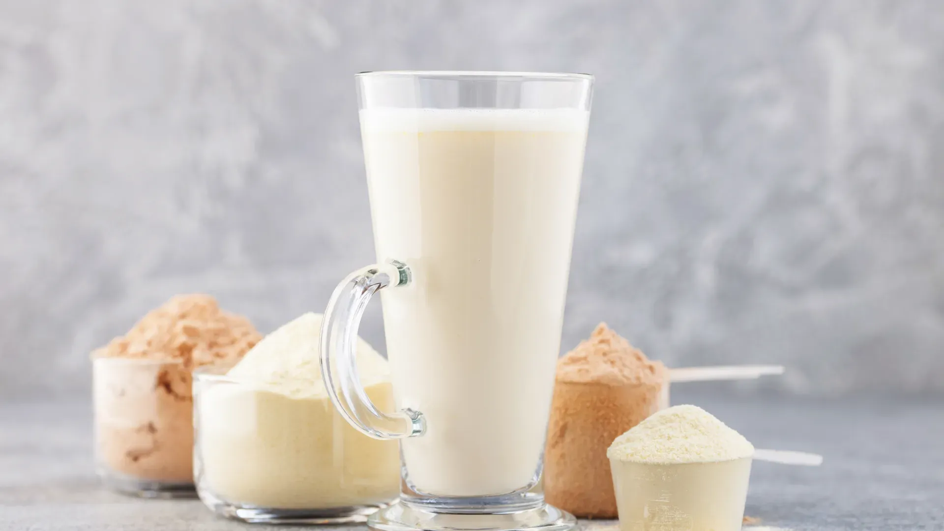 Um copo cheio de bebida, cercado por quatro scoops de Whey Protein