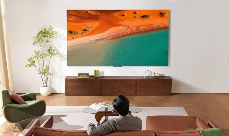 Foto mostra homem sentado em sofá e assistindo a TV TCL 85C8K em uma ampla sala