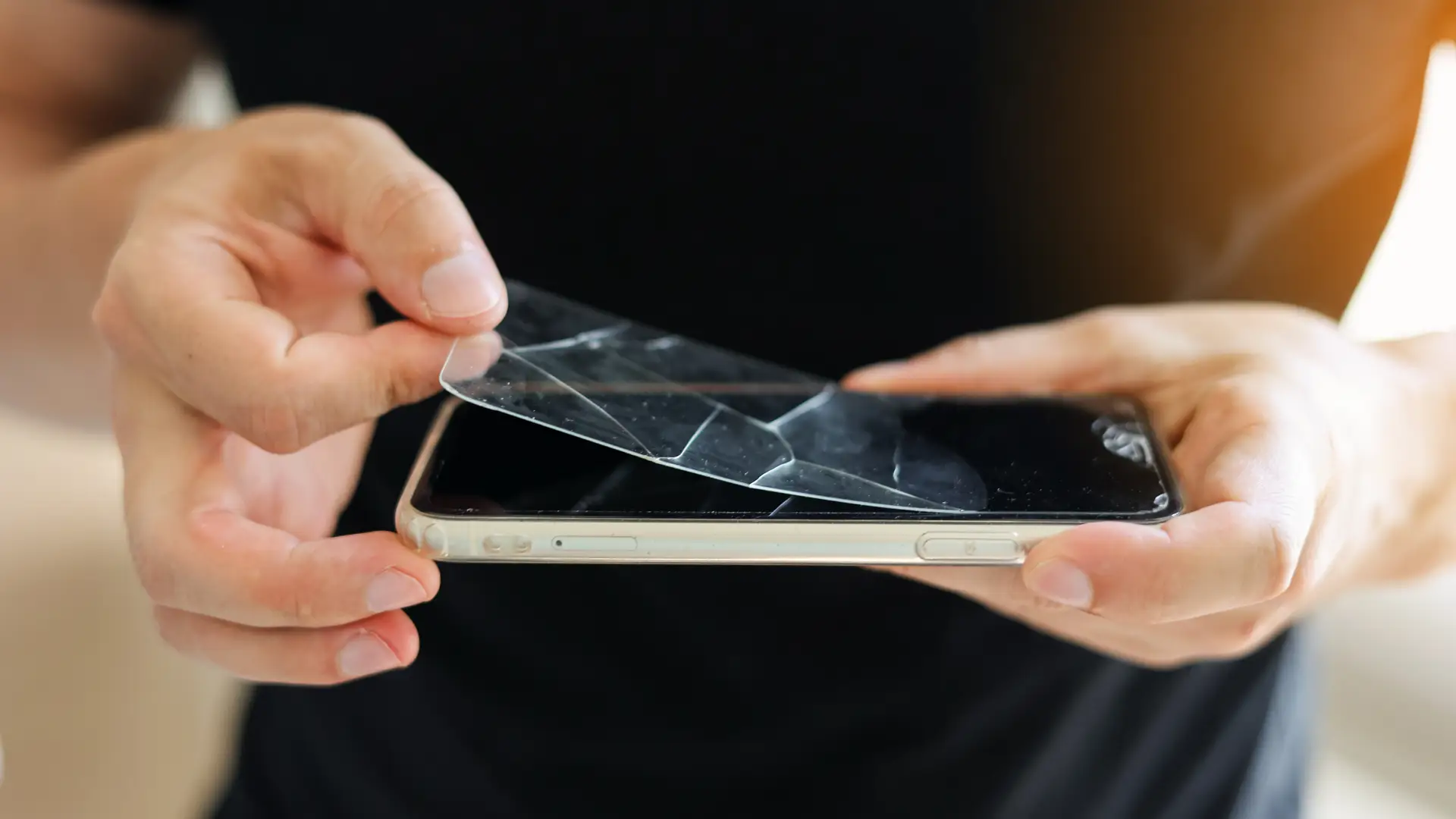 Imagem com zoom de duas mãos removendo uma película quebrada de um celular  