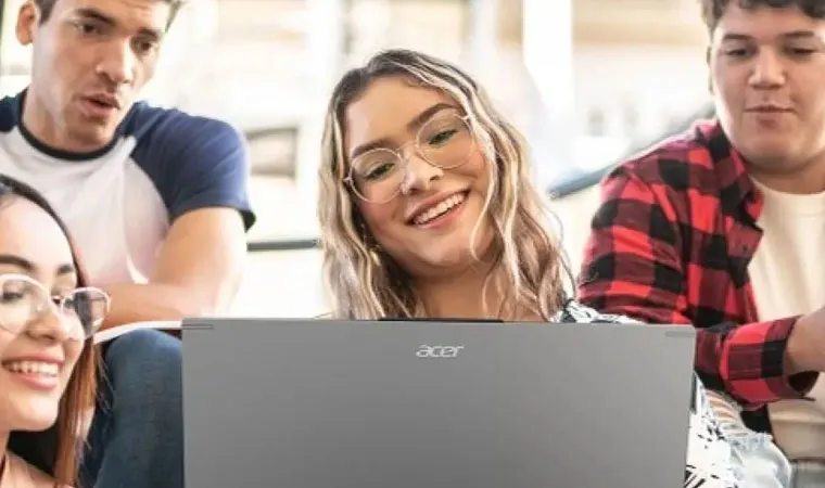 Foto de uma mulher loira com o notebook Acer Aspire 16 no colo enquanto outras pessoas ao fundo olham para a tela 