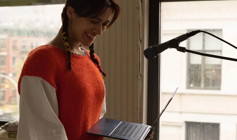 Imagem de uma artista de blusa laranja à esquerda segurando um MacBook Air M2 