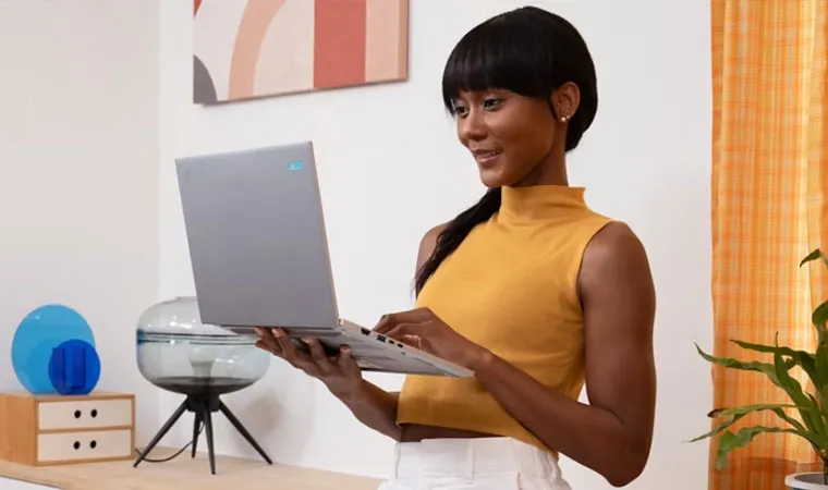Foto de uma mulher negra segurando o Acer Aspire 16 em uma das suas mãos enquanto usa o painel de toque com a outra 