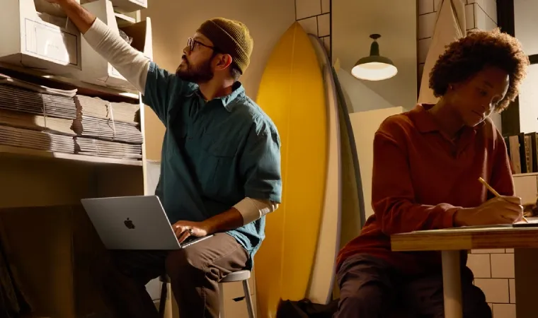 Imagem mostra um homem trabalhando com um MacBook Air no colo, junto de uma mulher ao seu lado.