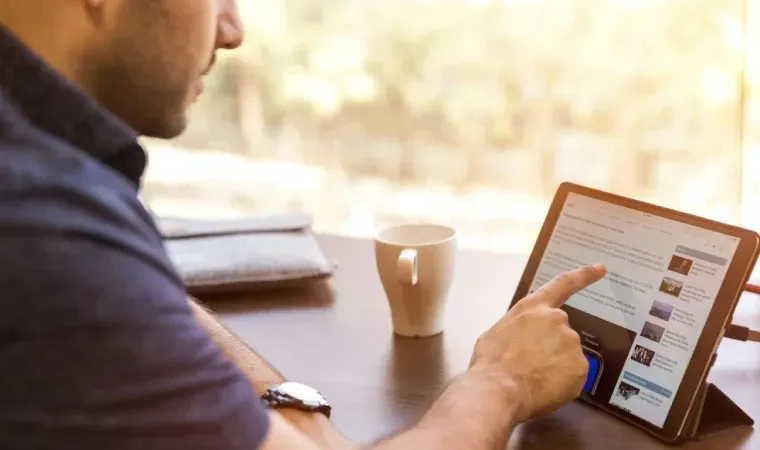 Imagem de um homem usando um tablet que está em cima de uma mesa