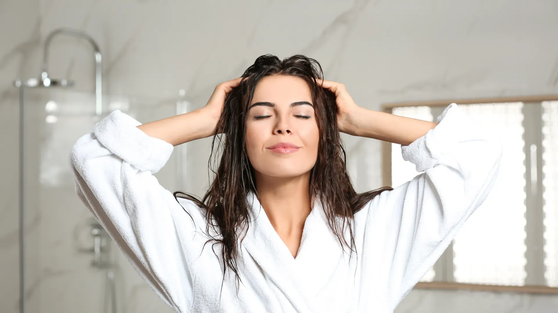 Em um banheiro, uma mulher branca, de cabelos escuros está massageando os fios