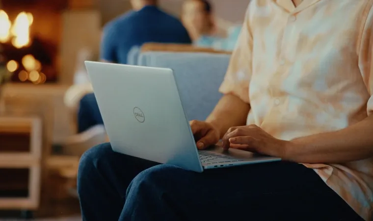 Imagem mostra um rapaz sentado no sofá utilizando um notebook com IA da Dell no colo.