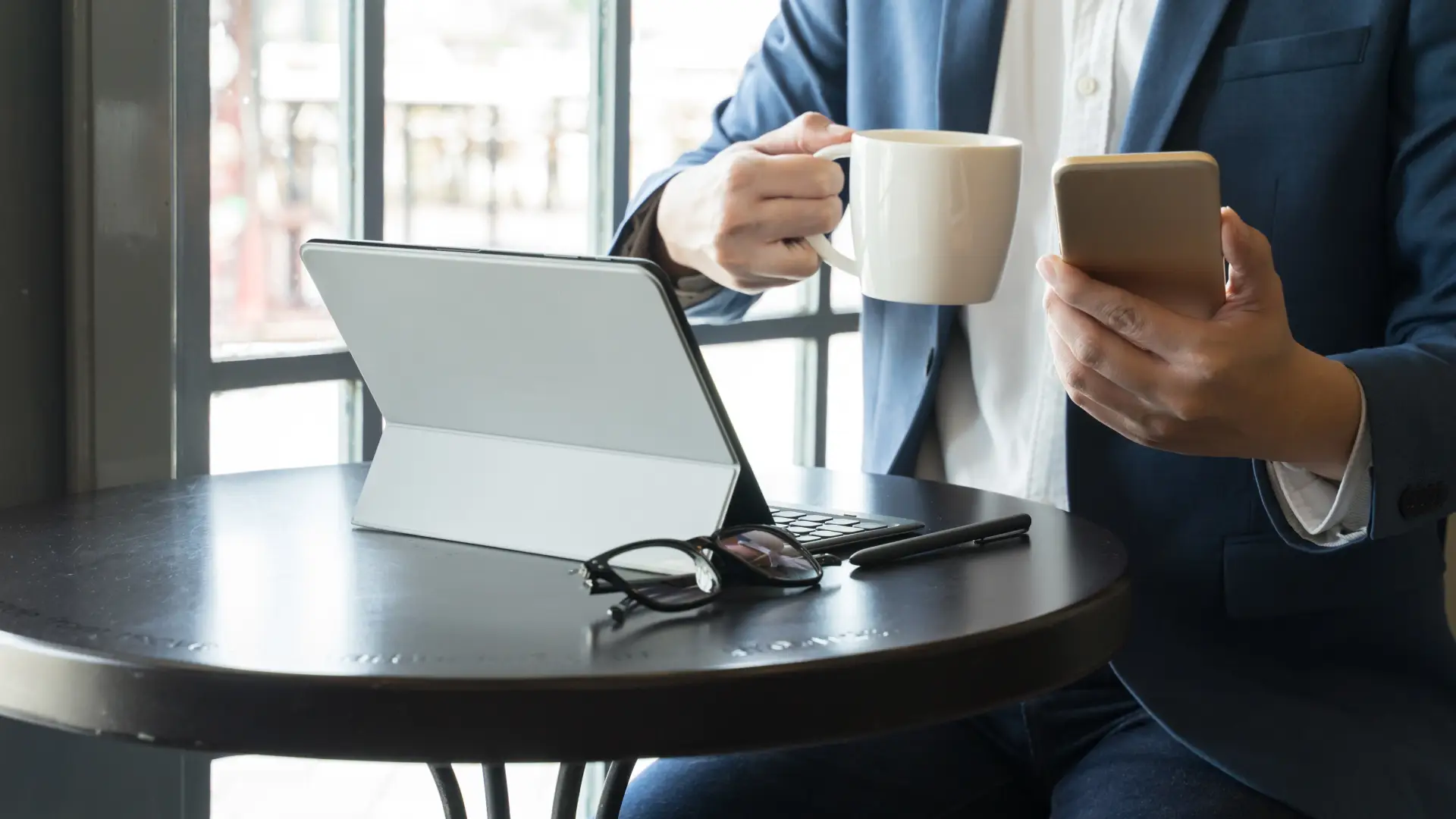 Uma pessoa está diante de um tablet com duas xícaras de café na mão
