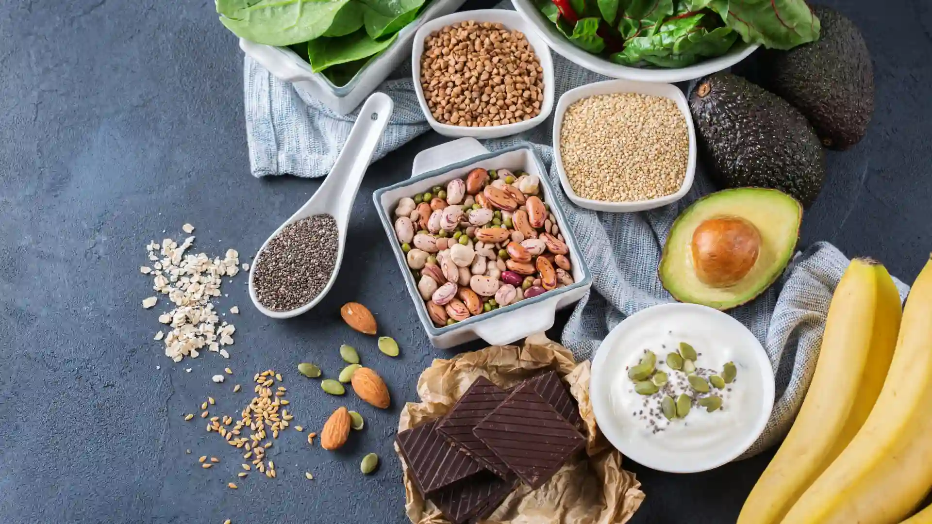 Em uma bancada estão dispostos alimentos que apresentam magnésio, como cacau, abacate e banana.