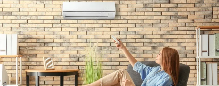 Jovem mulher branca sentada na poltrona ajustando a temperatura do ar-condicionado.