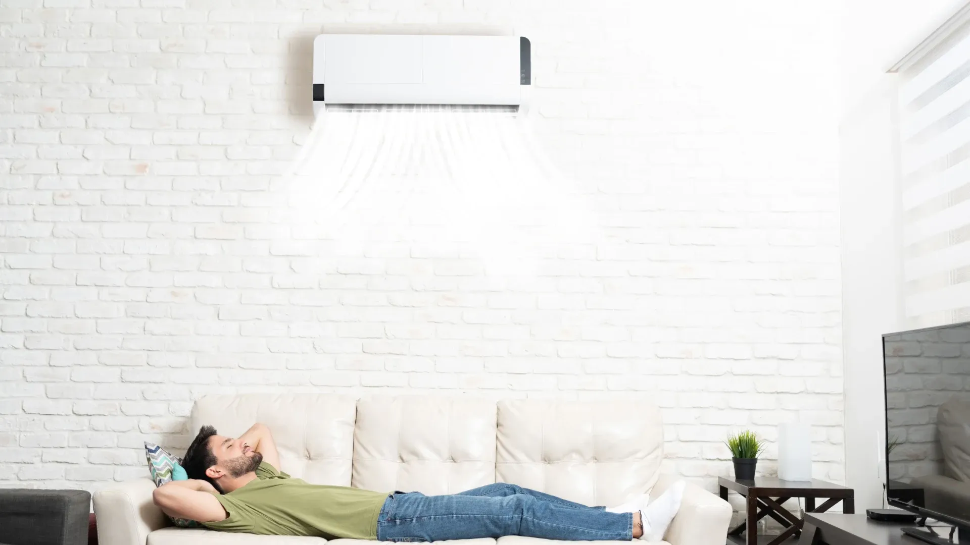 Homem deitado em sofa branco em cima tem um ar-condicionado split na parede