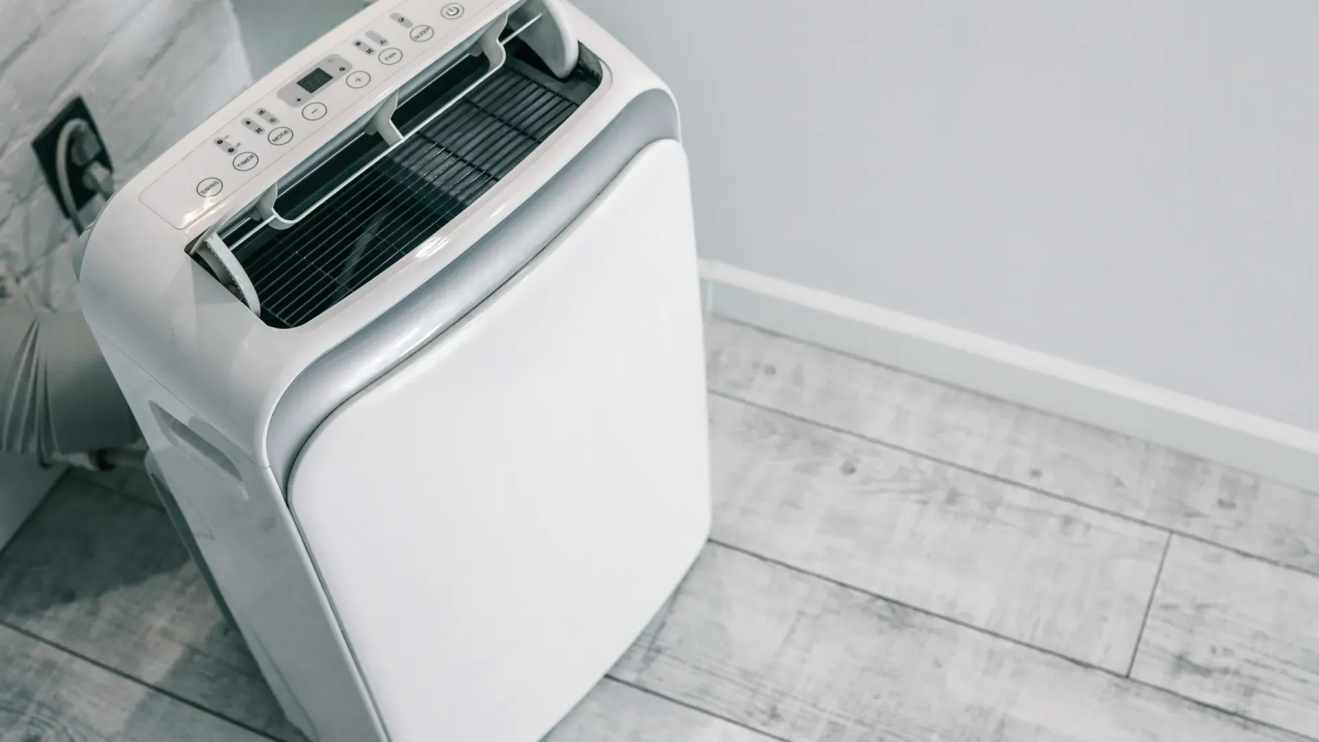 ar-condicionado portátil branco, no canto da sala próximo a uma tomada, com a tampa superior aberta