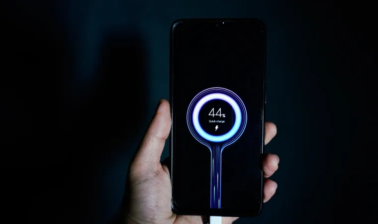 Imagem de uma pessoa segurando um celular que está carregando e, em sua tela, mostra a logo de carregamento  