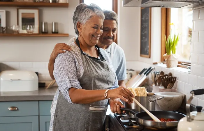 Duas pessoas cozinhando juntas em uma cozinha aconchegante, mexendo uma panela no fogão.