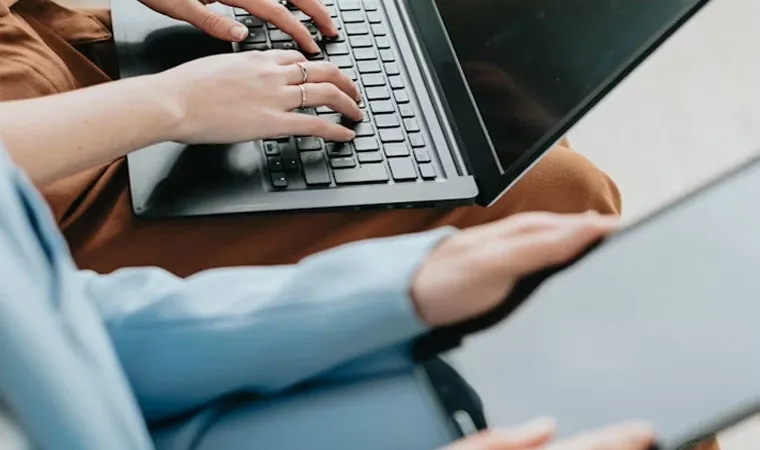 Imagem de duas pessoas sentadas, uma utilizando um notebook na parte de cima da imagem e outra usando um tablet abaixo