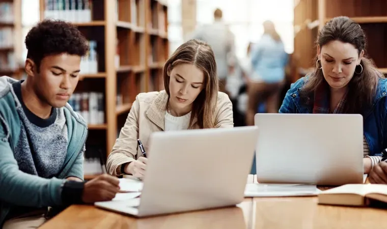 Imagem de estudantes em uma biblioteca estudando com dois notebooks na mesa