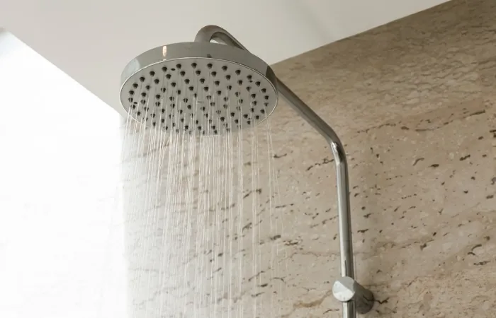 Chuveiro metálico liberando jatos de água em um banheiro revestido de pedra.