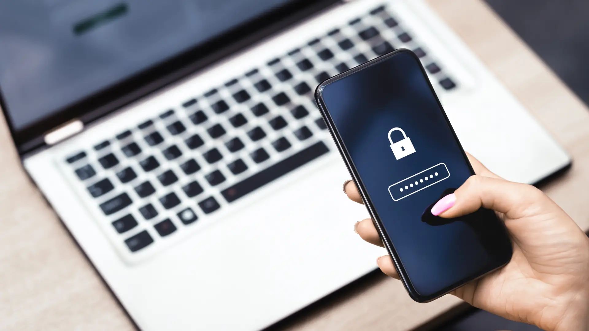Imagem de um celular com ícone de cadeado na tela sendo segurado por uma pessoa, com um notebook ao fundo, representando segurança e proteção de dados no smartphone.