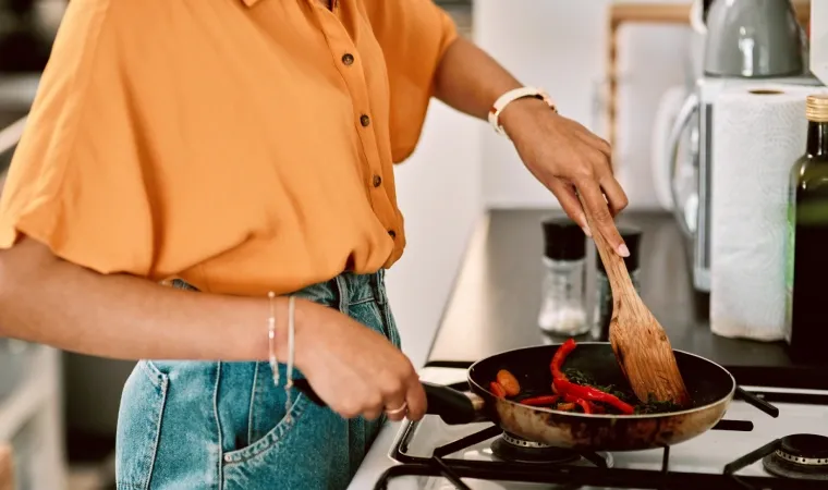 pessoa usa frigideira para fritar vegetais em fogão 5 bocas