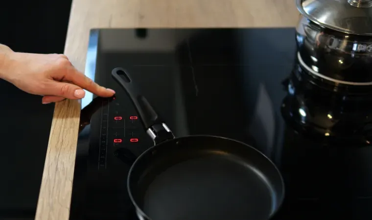 Mão feminina ligando cooktop com frigideira inox sobre uma das bocas