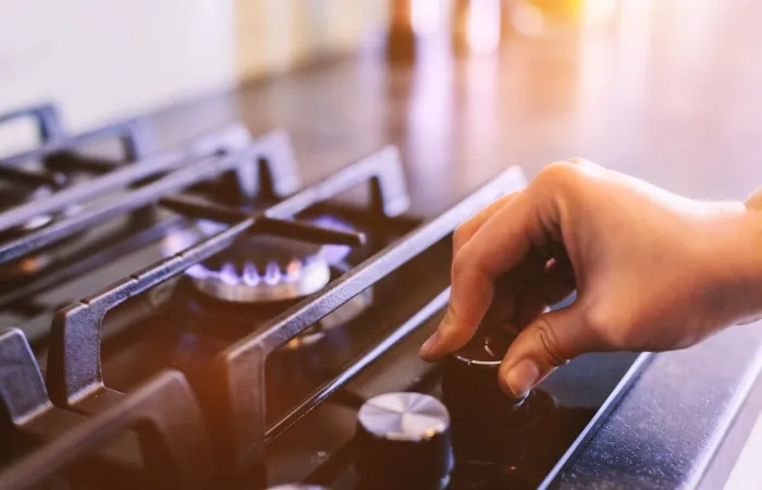 Mão girando o botão de acendimento de um fogão 5 bocas com mesa de vidro para acender o queimador.