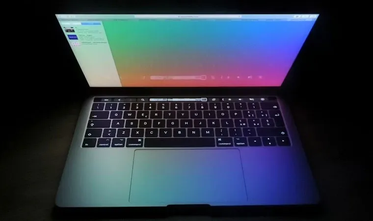 Imagem de um notebook semiaberto com uma imagem colorida emitindo luz sobre o teclado em um ambiente escuro
