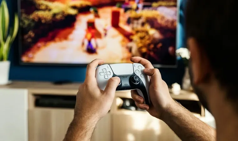 Foto de uma pessoa jogando um PlayStation 5 com um controle DualSense na mão e uma imagem desfocada do jogo Crash Bandicoot N.Sane Trilogy na tela