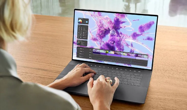 Foto de uma mulher de costas usando um notebook Dell XPS sobre uma mesa com uma arte roxa na tela