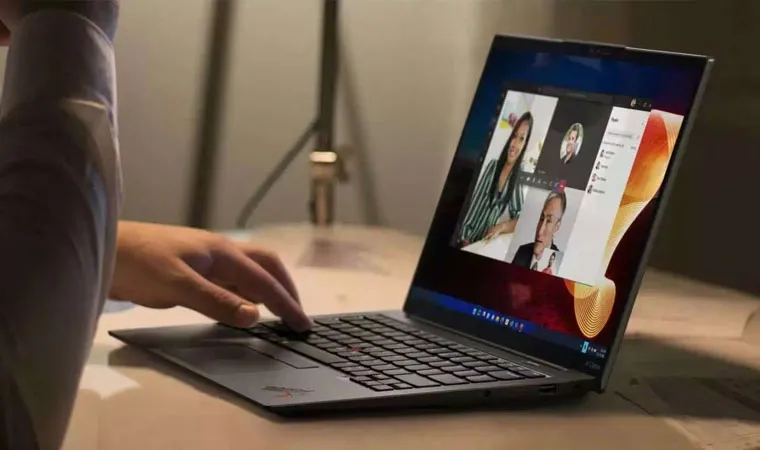 Foto de uma pessoa usando um Lenovo ThinkPad sobre uma mesa exibindo uma reunião na tela