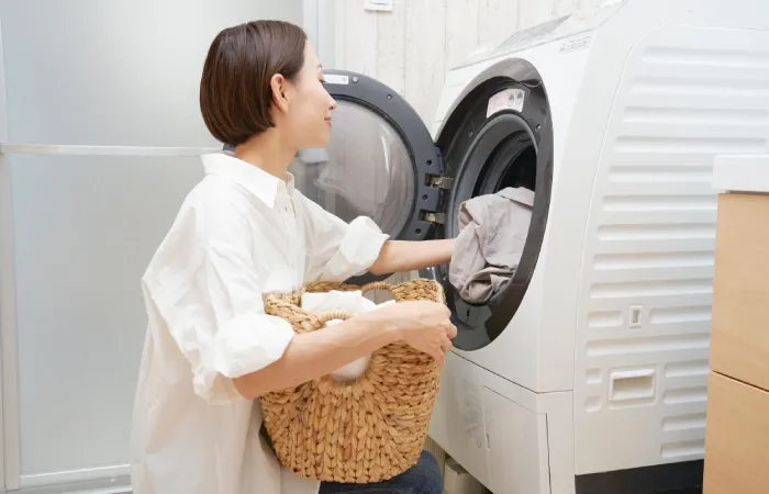 Pessoa colocando roupas em uma máquina de lavar, segurando um cesto de palha.