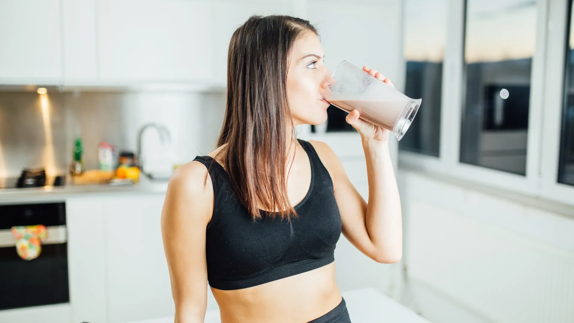 Jovem mulher branca bebendo whey protein no copo