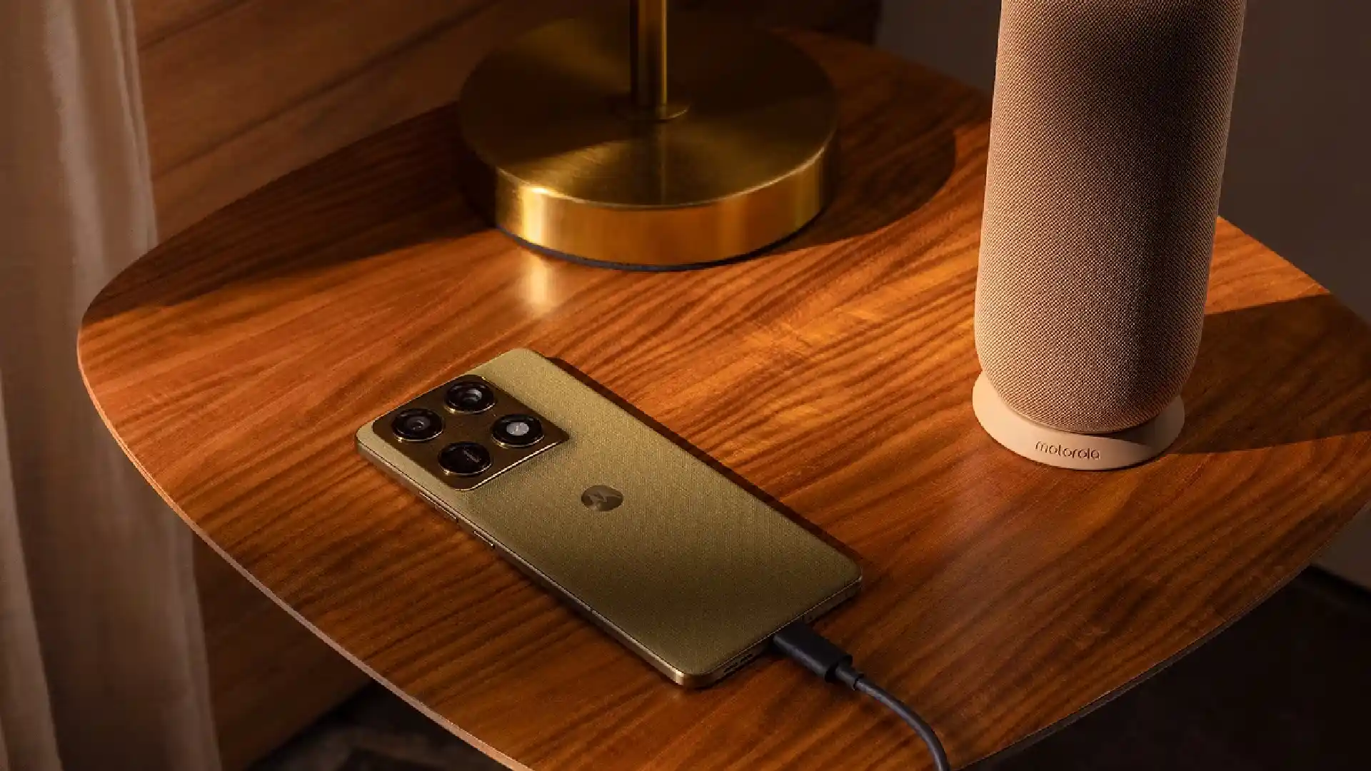 Motorola Signature carregando sobre mesa de madeira ao lado de caixa de som, ilustrando a autonomia de bateria do aparelho