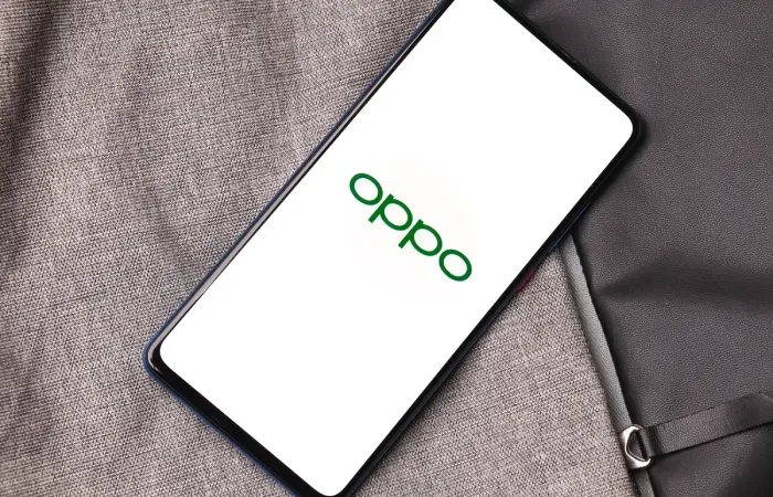 Celular Oppo com a tela branca e a logo da fabricante em verde sobre tecido cinza