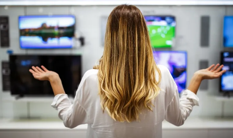 Mulher de costas em loja de eletrônicos observa variados aparelhos de TV.