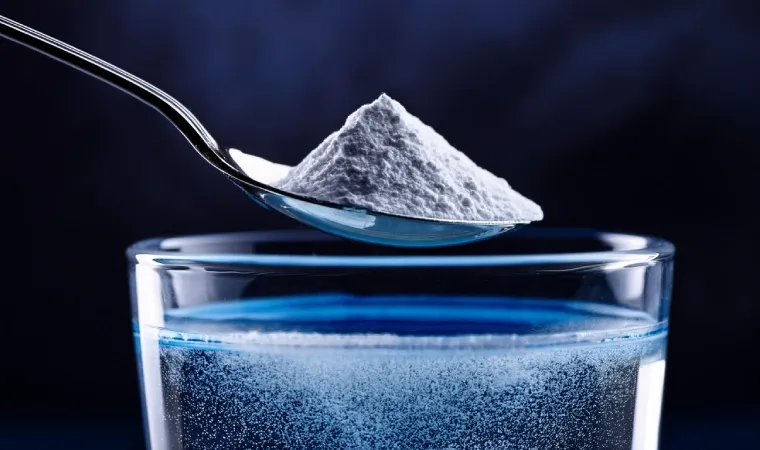 uma colher de sopa cheia de creatina athletica em pó em cima de um copo com água