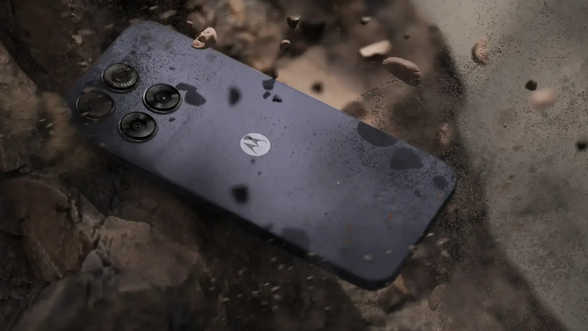 Smartphone Moto G67 em superfície rochosa com poeira, evidenciando robustez e câmera de 50MP
