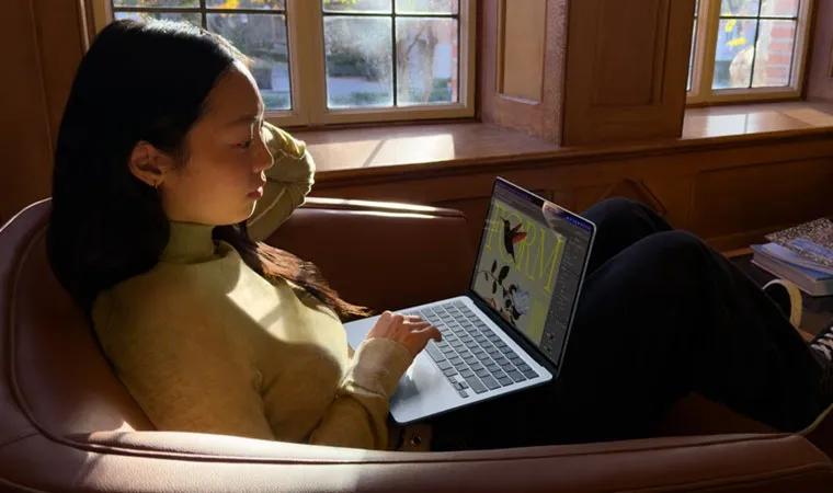 Foto de uma mulher sentada em uma cadeira usando um MacBook Air com M5 em seu colo