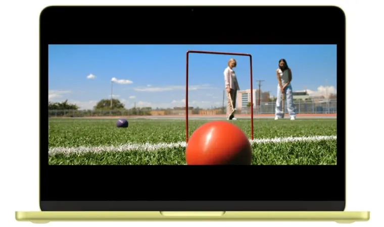 Imagem de um MacBook Neo aberto exibindo a série Pluribus da Apple TV com duas personagens jogando Croquet com foco em uma bola vermelha