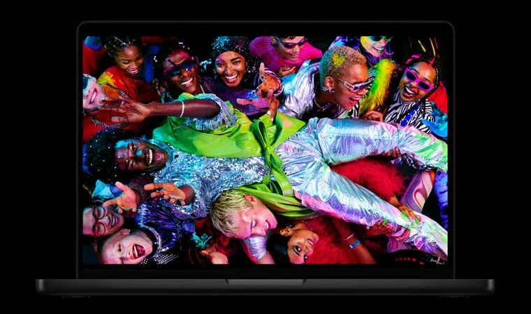 Imagem de um MacBook Pro M5 aberto mostrando uma festa com pessoas de roupas coloridas carregando uma pessoa acima das outras