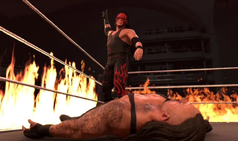 Imagem do jogo WWE 2K26 com o personagem Kane de pé em frente ao lutador Undertaker caído no ringue com um fundo de chamas