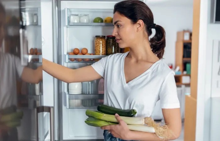 Mulher pegando alimentos saudáveis dentro da geladeira na cozinha