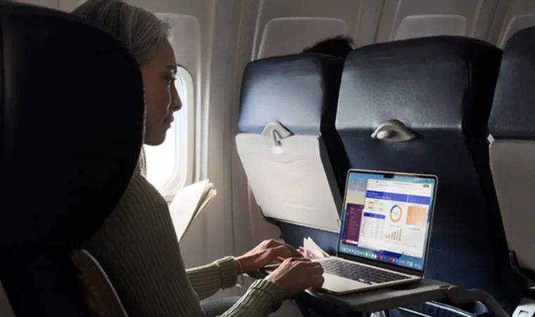 Mulher usando o MacBook Air M5 em um avião com o notebook aberto sobre a bandeja da poltrona
