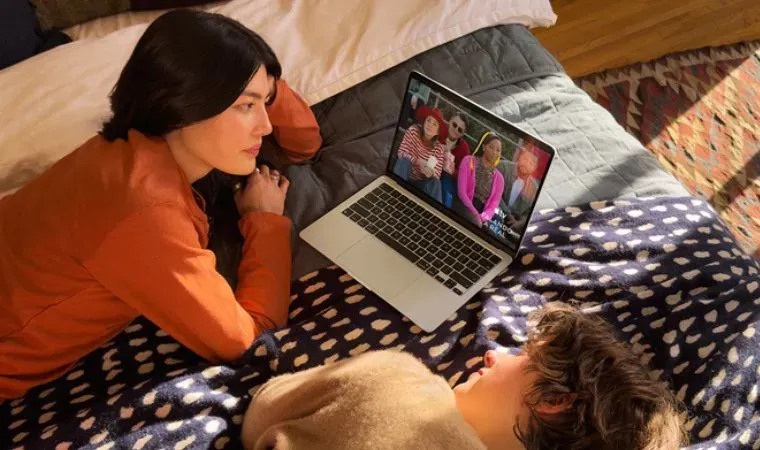 Homem e mulher jovens deitados na cama assistem filme com conforto em um O MacBook Air M5