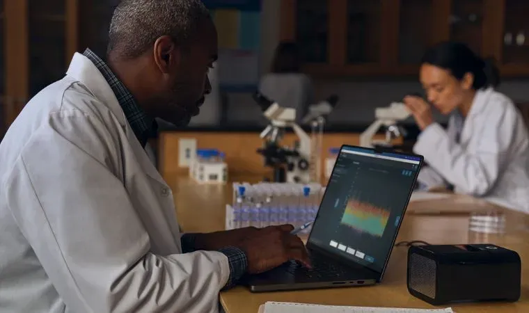 Cientistas em um laboratório com microscópio e ampolas trabalham com gráficos em um notebook Apple Macbook Pro M4